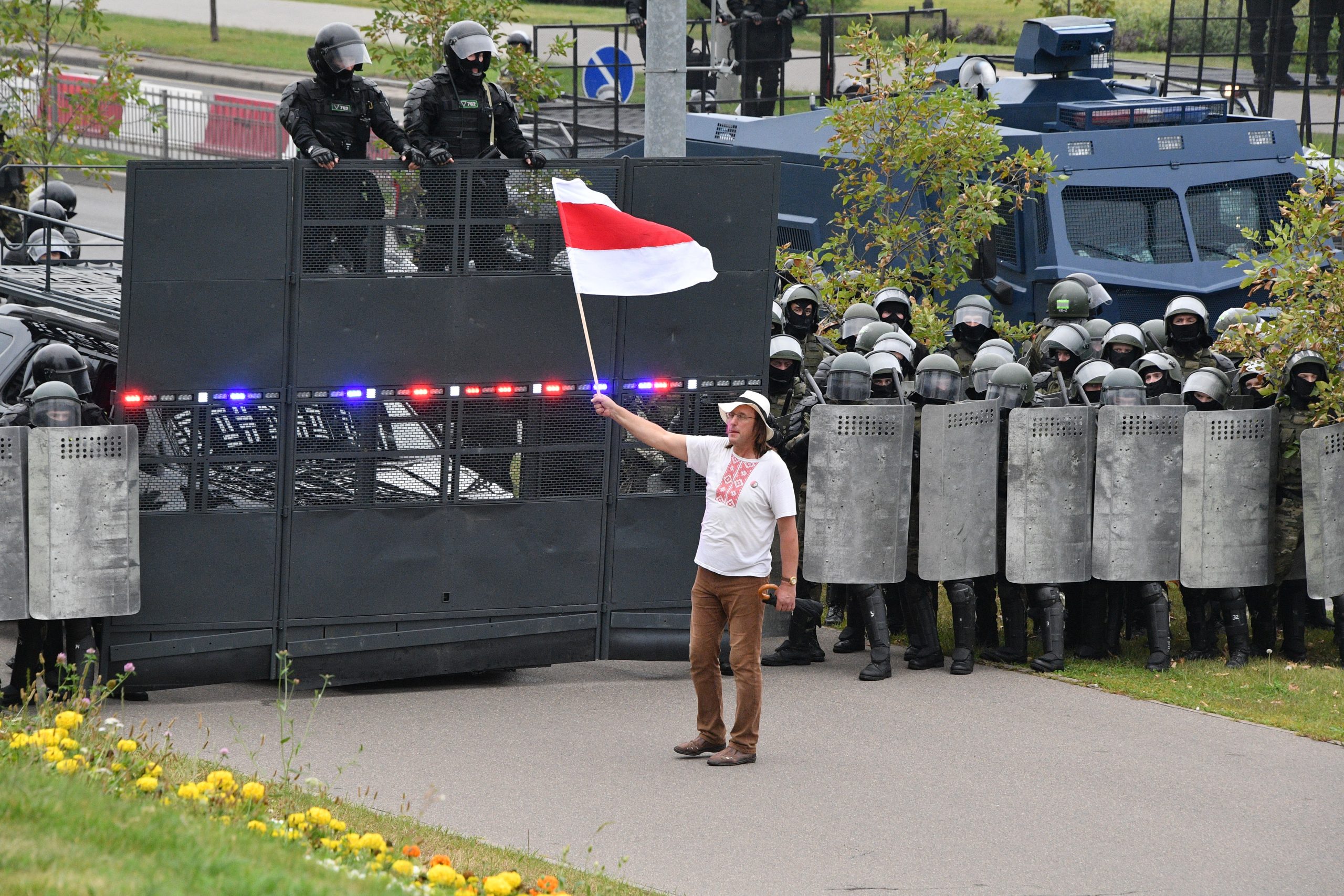  Недавно умерший за решеткой художник Алесь Пушкин держит бело-красно-белый флаг перед бойцами ОМОН на акции протеста. Лето 2020 года. Фото: belsat.by.