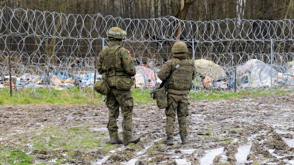 Польские пограничники смотрят на лагерь нелегальных мигрантов на беларуской стороне в в Беловежской пуще. Фото: rp.pl.